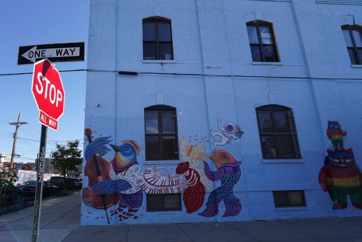 A blue painted building in Brooklyn, NYC. Graffitis of animals playing musical instruments are painted on the building. A stop street sign is visible in front of the building.