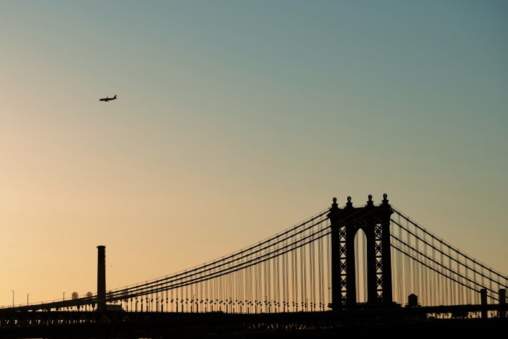 Silouhette of a plane in the sky, preparing to land, seen above the Brooklyn bridge, at dusk.