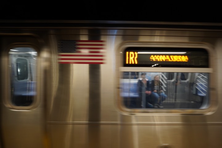 Motion blurred picture of the NYC subway passing by. The subway is going towards the left. A couple of people can be seen through the window.